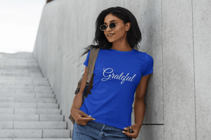 Grateful-tee-in-blue-soft-ringspun-cotton-by-CP-Designs-Unlimited-worn-by-young-woman-leaning-on-wall-smiling